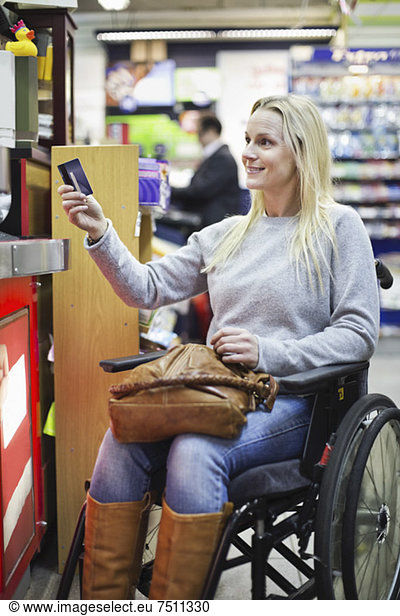 Disabled woman in wheelchair paying through credit card at supermarket