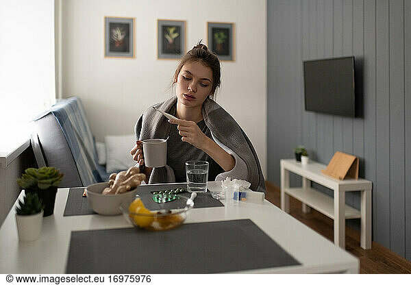 Diseased woman drinking tea and measuring temperature