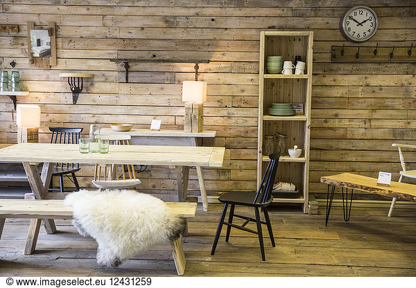 Display of furniture made from recycled wood  including dining table and bench  bookshelf and chair  wooden floor and wall.