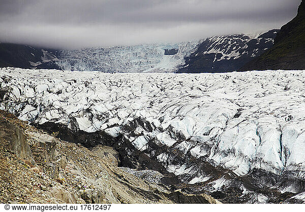 Distant hikers dwarfed by a massive Icelandic glacier.; Svinafellsjokull Glacier  Skaftafell National Park  Iceland.