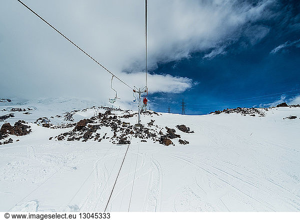 Distant view of man on ski lift against cloudy sky during winter