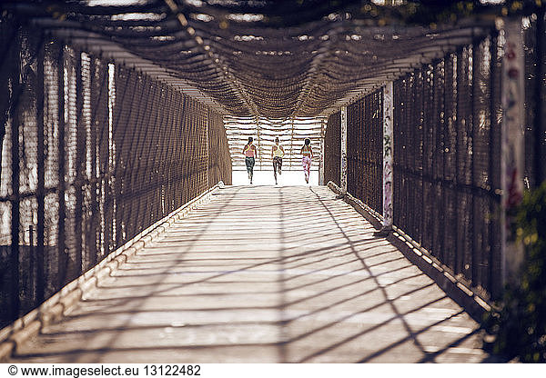 Distant view of sportswomen jogging on bridge on sunny day