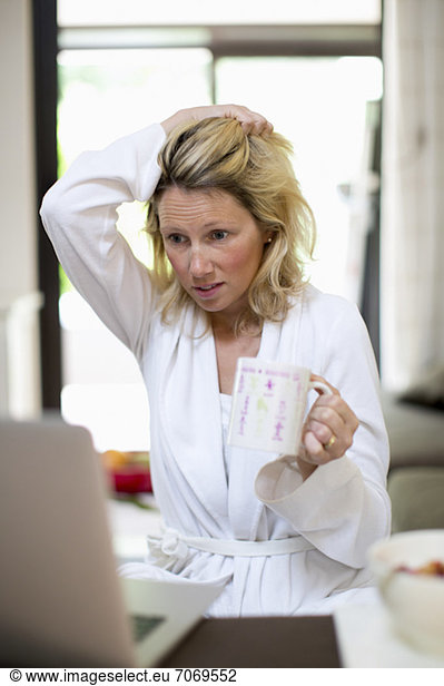 Distraught woman with coffee cup working on laptop at home