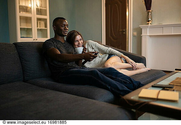 Diverse couple cuddling on sofa and watching TV together