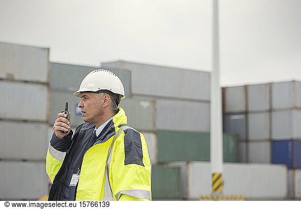 Dock manager with walkie-talkie among cargo containers at shipyard