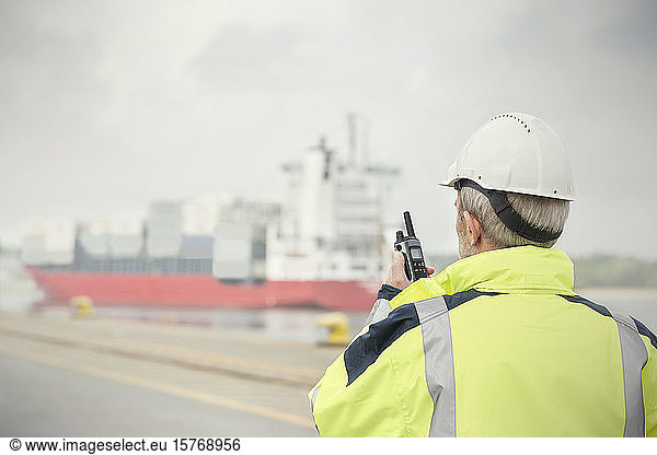 Dock manager with walkie-talkie watching container ship at commercial dock