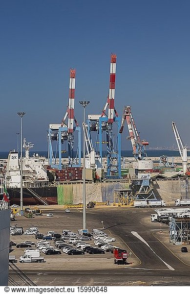 Dock with parked motor vehicles ready for shipping plus docked cargo ship and shipping container loading cranes in background  Ashdod Port  Israel.