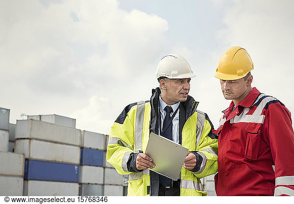 Dock worker and manager with clipboard talking at shipyard