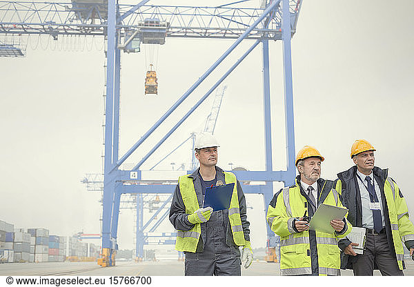 Dock workers and manager walking below crane at shipyard