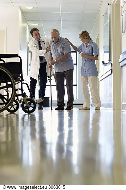 Doctor and nurse helping older patient walk in hospital