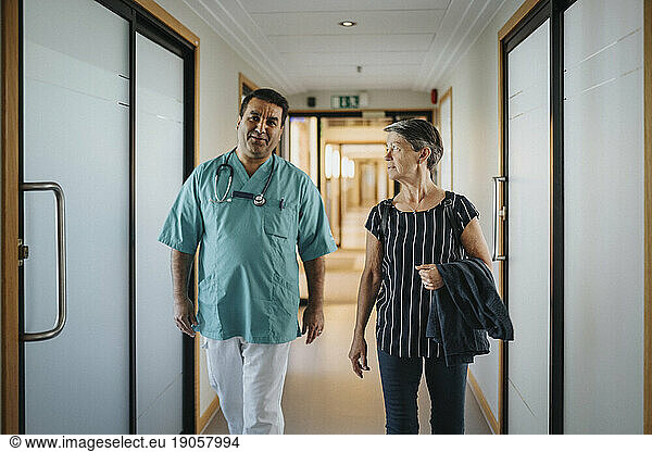 Doctor discussing with senior patient while walking in corridor of hospital