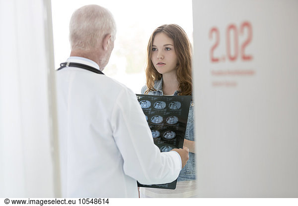 Doctor discussing x-rays with serious teenage patient in examination room