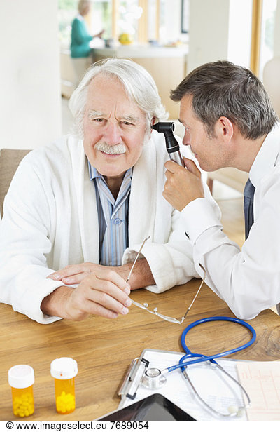 Doctor examining older man's ear at house call