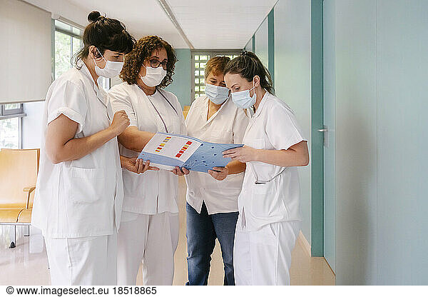Doctor explaining medical report to colleagues standing at hospital corridor
