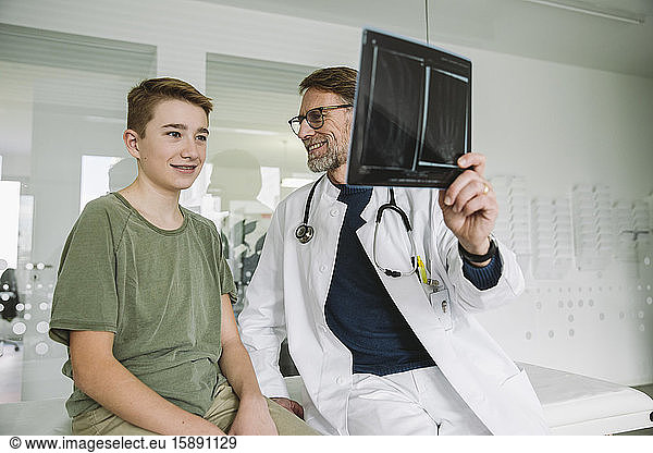 Doctor explaining x-ray image of broken hand to teenage boy in medical practice