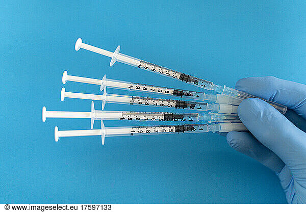 Doctor hand holding vaccine syringes against blue background