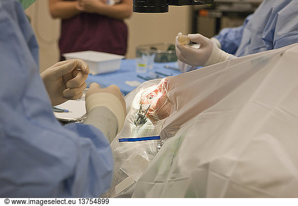 Doctor holding bulb syringe and patient under sterile drapes with eye retractor in eye