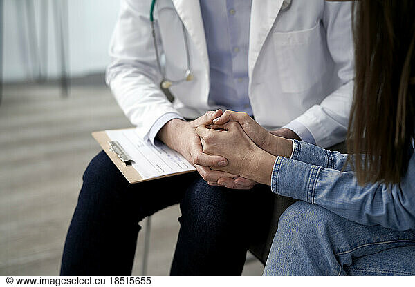 Doctor holding hands and consoling patient in clinic
