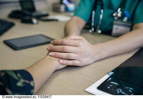 Doctor holding patient's hand on table