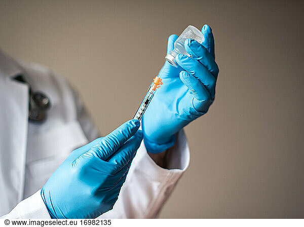 Doctor in white coat drawing vaccine into a syringe for injection.