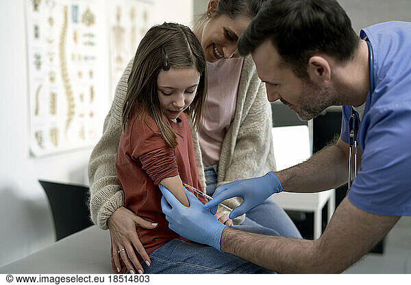 Doctor injecting syringe in girl's arm at clinic