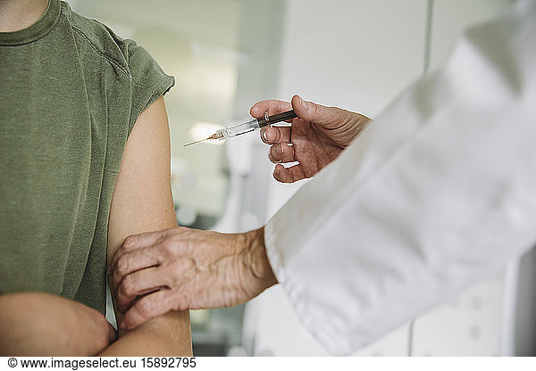 Doctor injecting vaccine into arm of teenager