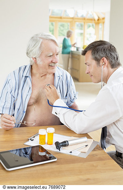 Doctor listening to older patient's heartbeat at house call