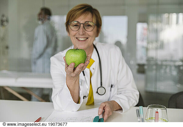 Doctor sitting at desk holding an apple