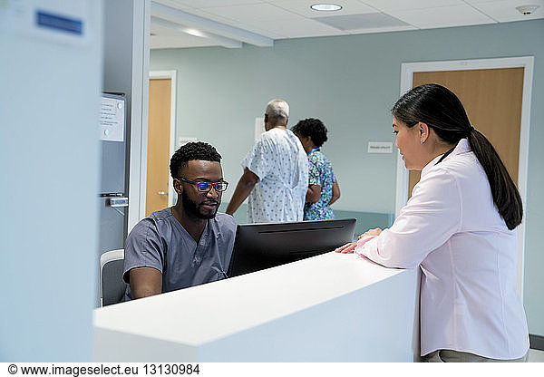 Doctor talking to male nurse at hospital reception while colleague with patient walking in background