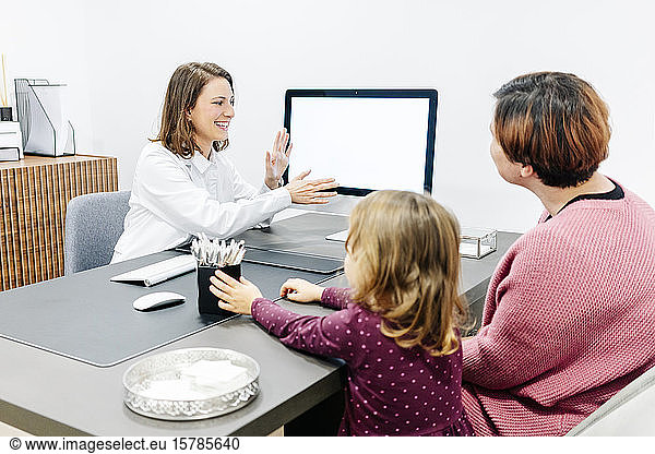 Doctor talking to mother with daughter at desk in medical practice