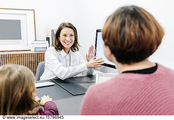 Doctor talking to mother with daughter at desk in medical practice