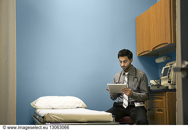Doctor using tablet computer while sitting on stool at hospital