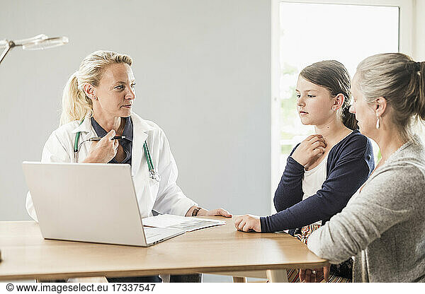 Doctor with laptop looking at patient and woman in office