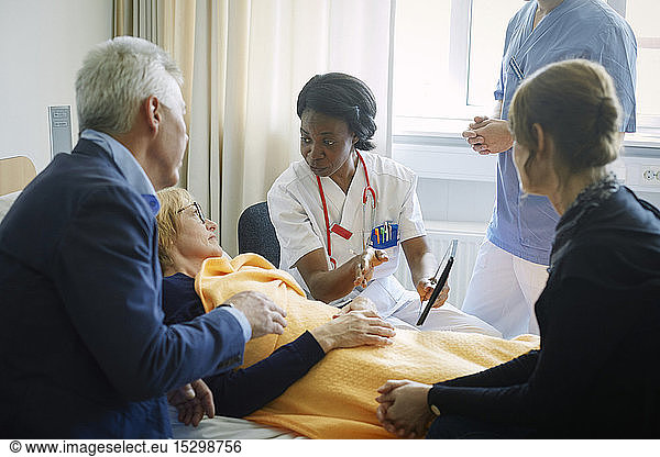 Doctor with nurse explaining mature patient and her friends at hospital ward