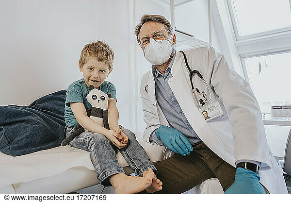 Doctor with protective face mask sitting by boy at examination room