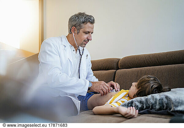 Doctor with stethoscope examining boy at home