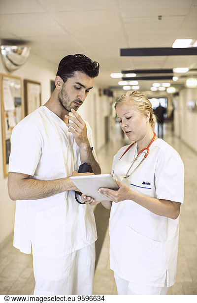 Doctors discussing over digital tablet in hospital corridor