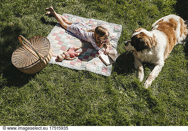 Dog and little girl lay on blanket in grass with basket and doll
