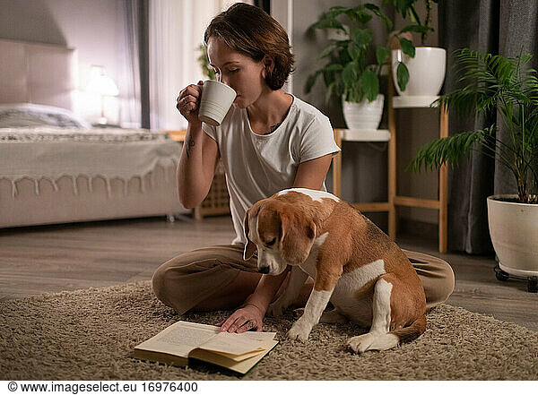 Dog owner drinking hot beverage and reading book