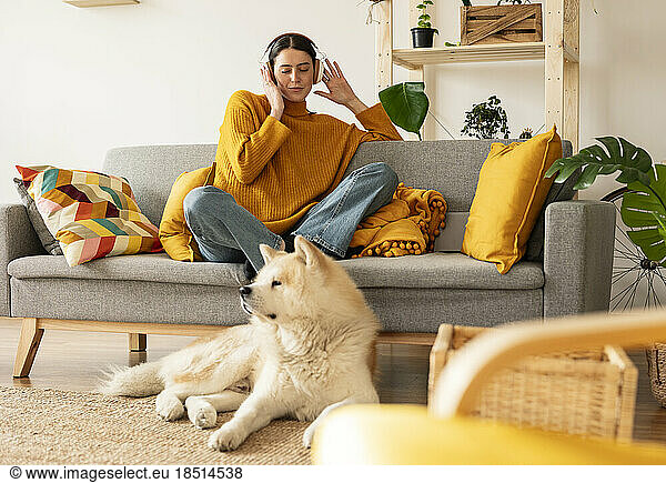 Dog sitting on carpet in front of young woman enjoying music at home