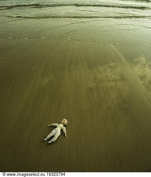 Doll lying on wet sandy beach at waterside