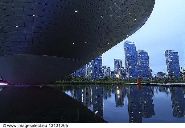 Dongdaemun Design Plaza by reflecting pool against sky in city at sunset