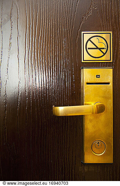 Door handle and no smoking sign on wooden door.