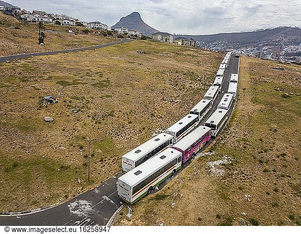 Doppelreihe von Bussen  die an einem Hang geparkt sind und als Transportlager genutzt werden. In der Ferne ist der ikonische Lion's Head zu sehen  ein Teil des Tafelbergs in Kapstadt  Südafrika.