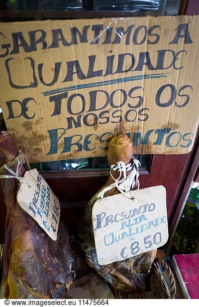 Dos Jamones colgados en una tienda de ultramarinos con un cartel escrito a mano que dice 'Garantimos a Qualidad de todos os nossos Presuntos. Ponte de Lima  Distrito de Viana do Castelo  Alto Minho  Portugal  Europa.