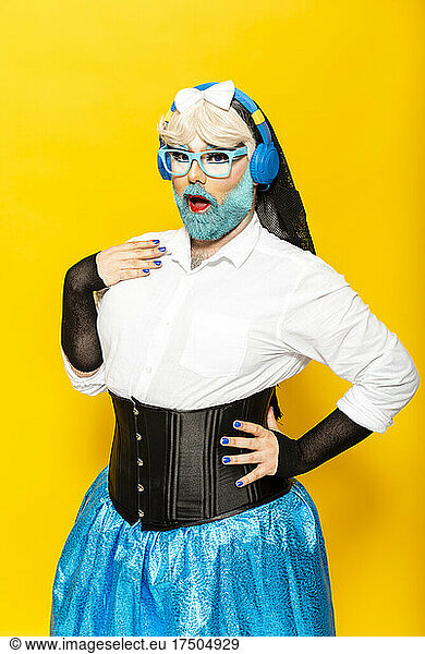 Drag Queen wearing headphones and eyeglasses in front of yellow background
