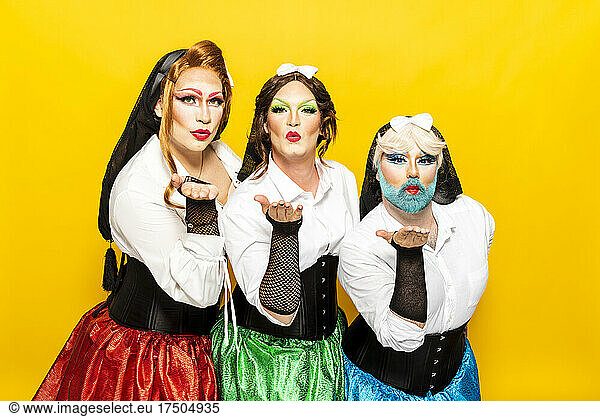 Drag queens giving flying kiss in front of yellow background