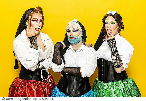 Drag queens wearing fishnet gloves making face against yellow background