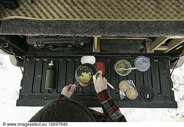 Draufsicht auf eine Frau  die im Kofferraum eines Geländewagens Essen zubereitet