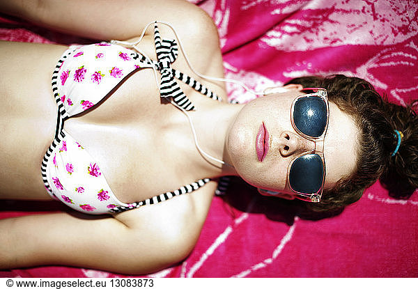 Draufsicht einer Frau im Bikini-Oberteil  die auf einem Strandtuch liegend ein Sonnenbad nimmt